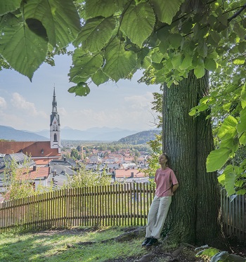 Zur Ruhe kommen und Kraft tanken. eine Frau lehnt an einem mächtigen Baumstamm über der Stadt Bad Tölz